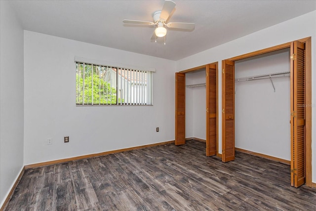 unfurnished bedroom featuring ceiling fan, dark hardwood / wood-style flooring, and two closets