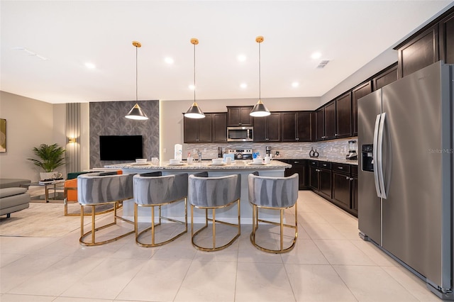 kitchen featuring appliances with stainless steel finishes, backsplash, dark brown cabinetry, decorative light fixtures, and a breakfast bar area