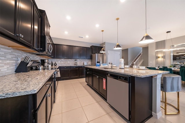 kitchen with decorative light fixtures, stainless steel appliances, and an island with sink