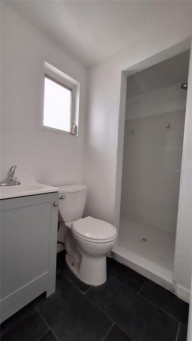 bathroom with toilet, vanity, tile patterned flooring, and a tile shower