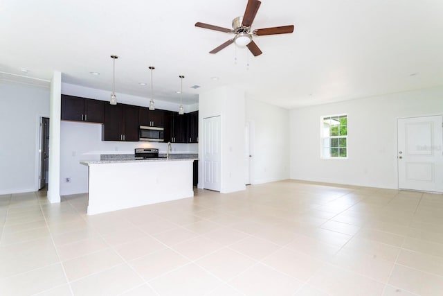 kitchen featuring an island with sink, appliances with stainless steel finishes, light tile patterned floors, pendant lighting, and light stone counters