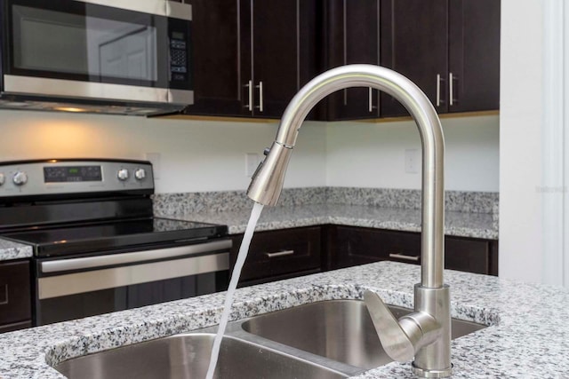 kitchen featuring stainless steel appliances, light stone countertops, and dark brown cabinetry