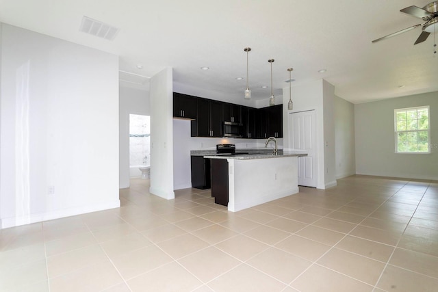 kitchen featuring hanging light fixtures, a center island with sink, ceiling fan, light tile patterned floors, and black range