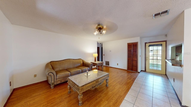 living room featuring light hardwood / wood-style flooring, a textured ceiling, and ceiling fan