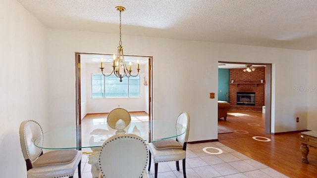 dining room with light hardwood / wood-style floors, a textured ceiling, ceiling fan with notable chandelier, and a brick fireplace