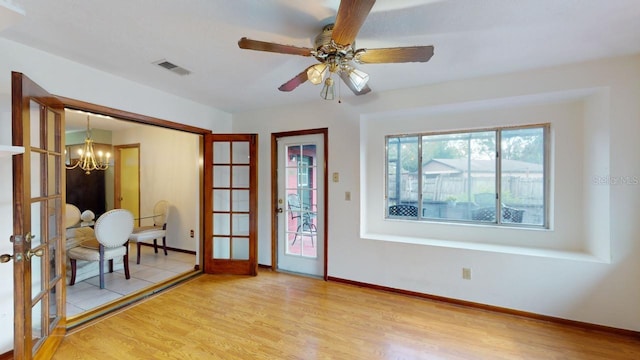 empty room featuring french doors, ceiling fan with notable chandelier, and light wood-type flooring