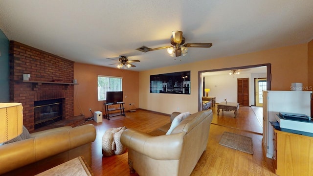 living room featuring a brick fireplace, light wood-type flooring, and ceiling fan