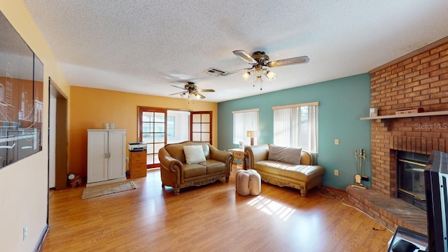 living room featuring a textured ceiling, a fireplace, light hardwood / wood-style floors, and ceiling fan