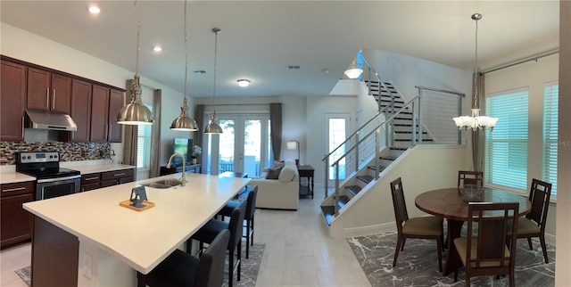 kitchen featuring tasteful backsplash, a center island with sink, stainless steel electric range oven, dark brown cabinetry, and sink