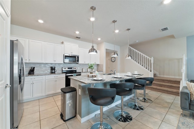 kitchen featuring a breakfast bar area, an island with sink, hanging light fixtures, stainless steel appliances, and white cabinets