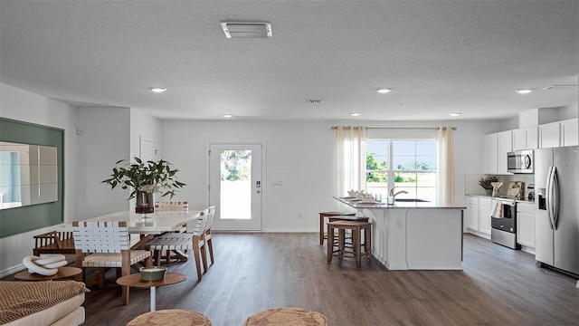 kitchen featuring white cabinets, stainless steel appliances, a wealth of natural light, and an island with sink