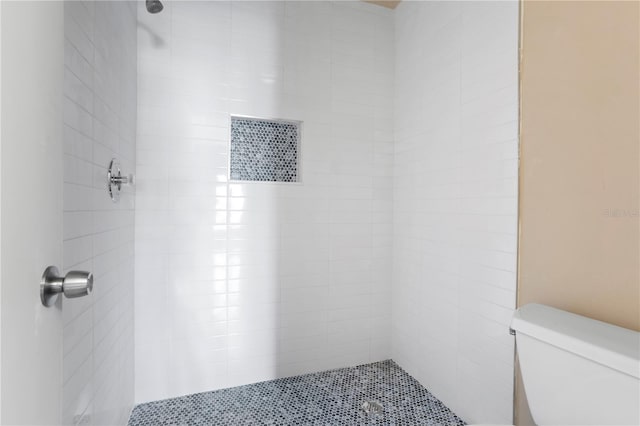 bathroom with a tile shower and toilet