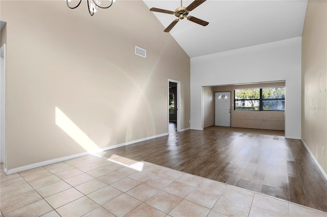 unfurnished living room with high vaulted ceiling, light wood-type flooring, and ceiling fan with notable chandelier