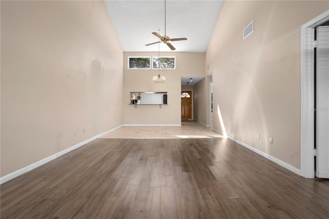 unfurnished living room featuring ceiling fan with notable chandelier, wood-type flooring, and high vaulted ceiling