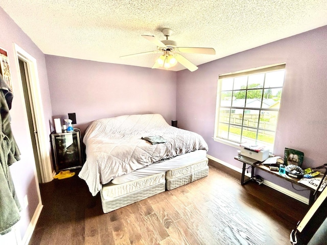 bedroom with a textured ceiling, wood-type flooring, and ceiling fan