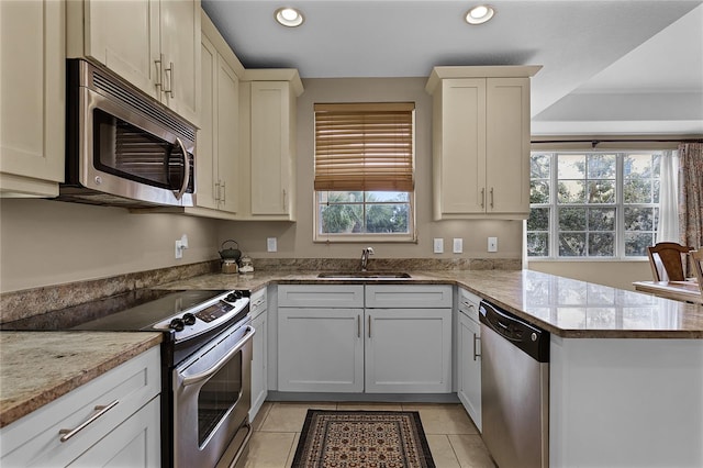 kitchen with kitchen peninsula, stainless steel appliances, sink, light stone countertops, and light tile patterned flooring