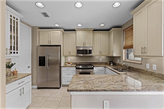 kitchen featuring sink, kitchen peninsula, stainless steel appliances, light stone counters, and light tile patterned floors