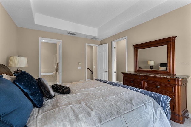 bedroom featuring connected bathroom, light carpet, and a raised ceiling