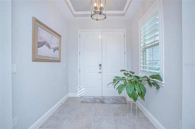 tiled entrance foyer featuring a notable chandelier, ornamental molding, and a tray ceiling