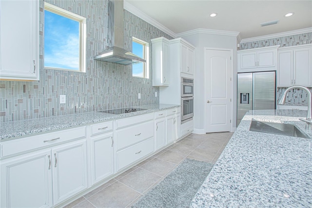 kitchen with white cabinetry, a healthy amount of sunlight, wall chimney range hood, and ornamental molding