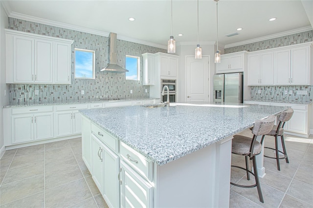 kitchen featuring wall chimney exhaust hood, appliances with stainless steel finishes, white cabinets, and an island with sink