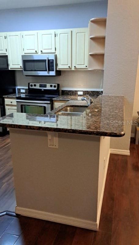 kitchen with kitchen peninsula, stainless steel appliances, sink, dark stone countertops, and white cabinetry