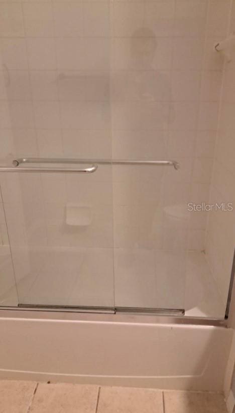 bathroom featuring tile patterned flooring and bath / shower combo with glass door