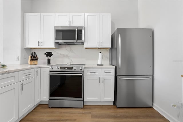 kitchen featuring wood finished floors, decorative backsplash, stainless steel appliances, light countertops, and white cabinetry