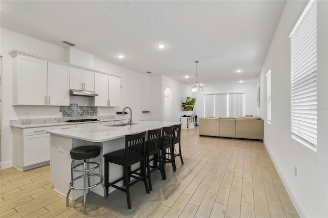 kitchen with sink, light hardwood / wood-style flooring, white cabinets, a breakfast bar area, and an island with sink