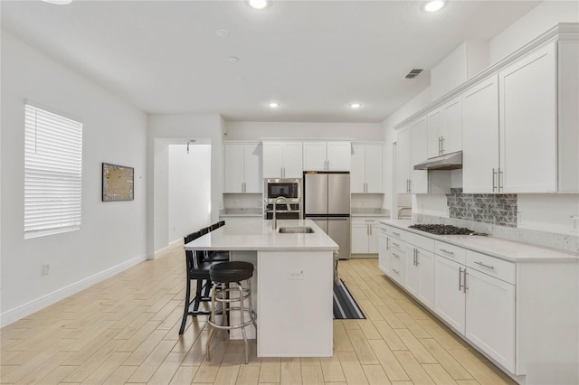 kitchen featuring a breakfast bar, stainless steel appliances, sink, white cabinetry, and an island with sink