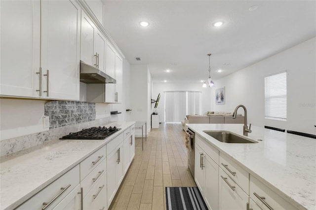 kitchen featuring light stone countertops, decorative light fixtures, white cabinetry, and sink