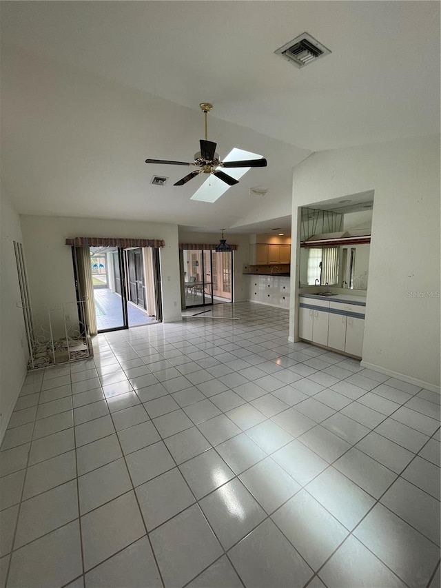 unfurnished living room with sink, ceiling fan, vaulted ceiling with skylight, and light tile patterned floors