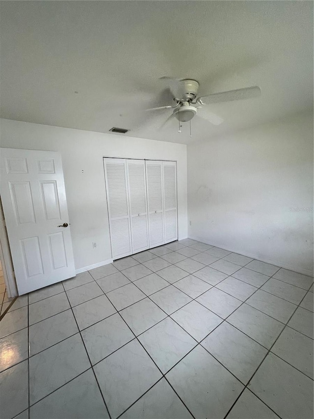 unfurnished bedroom with light tile patterned floors, a textured ceiling, a closet, and ceiling fan