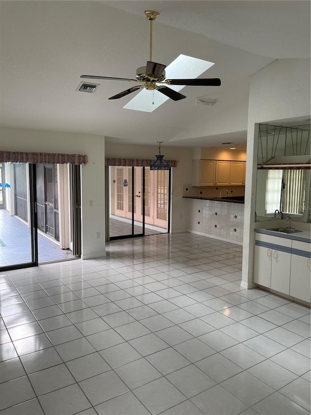 unfurnished living room featuring sink, vaulted ceiling with skylight, light tile patterned floors, and ceiling fan