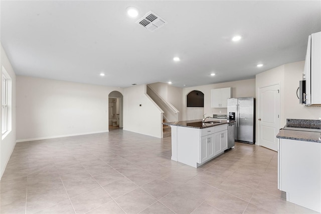 kitchen with appliances with stainless steel finishes, sink, dark stone countertops, white cabinets, and a kitchen island with sink