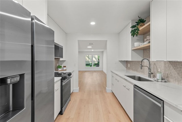 kitchen with appliances with stainless steel finishes, light hardwood / wood-style flooring, white cabinetry, and sink