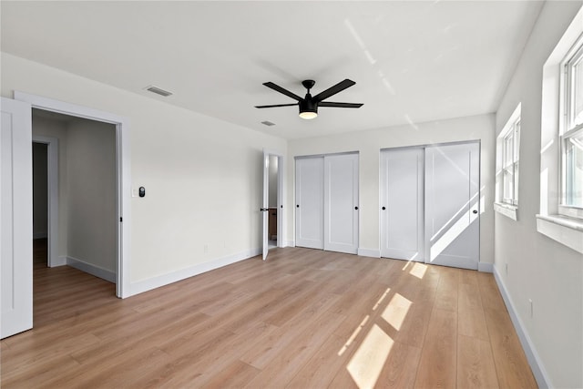 unfurnished bedroom with light hardwood / wood-style floors, two closets, and ceiling fan