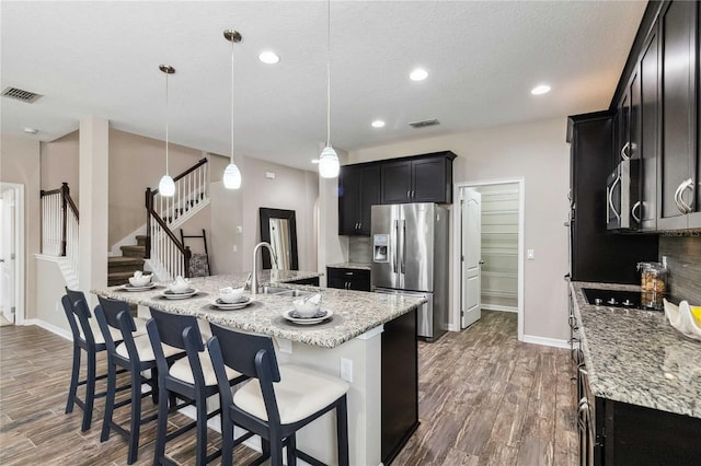 kitchen featuring sink, hanging light fixtures, stainless steel appliances, dark wood-type flooring, and a kitchen island with sink