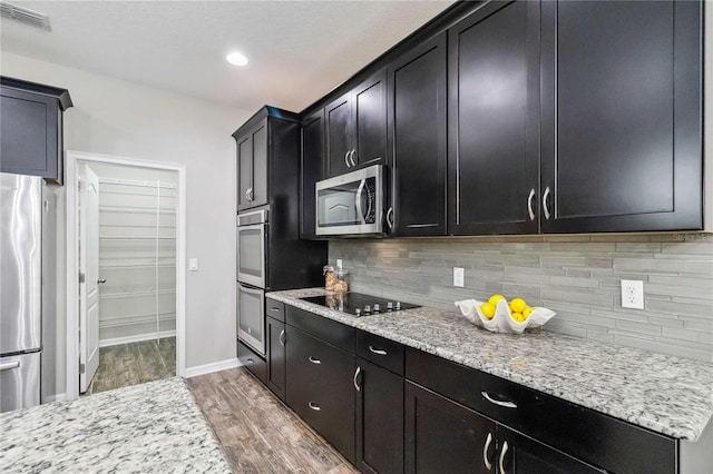 kitchen with light stone countertops, appliances with stainless steel finishes, hardwood / wood-style flooring, and backsplash