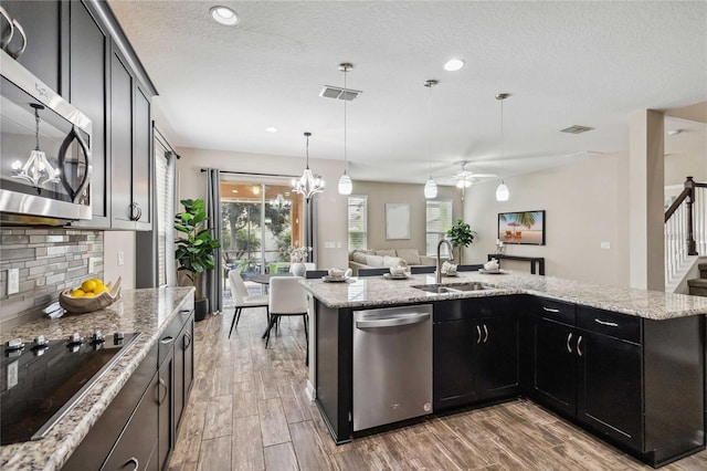 kitchen with wood-type flooring, sink, pendant lighting, appliances with stainless steel finishes, and light stone counters