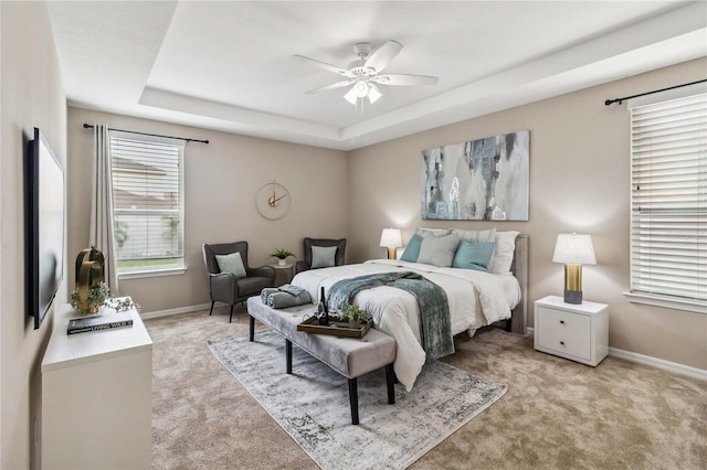 bedroom with ceiling fan, a tray ceiling, and light colored carpet