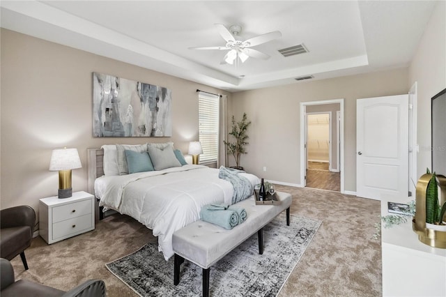 bedroom with connected bathroom, light carpet, a tray ceiling, and ceiling fan