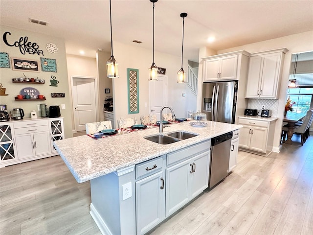 kitchen with sink, a kitchen island with sink, stainless steel appliances, and white cabinetry