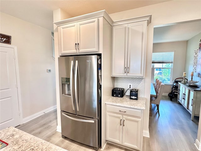 kitchen with light stone counters, tasteful backsplash, light hardwood / wood-style flooring, and stainless steel fridge