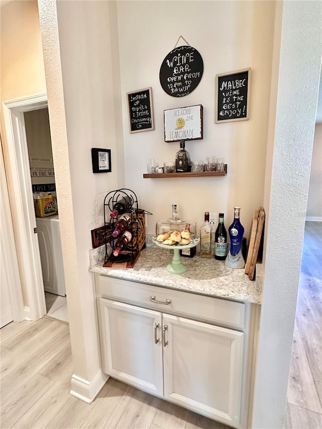 bar featuring washer / dryer, light stone countertops, and light wood-type flooring