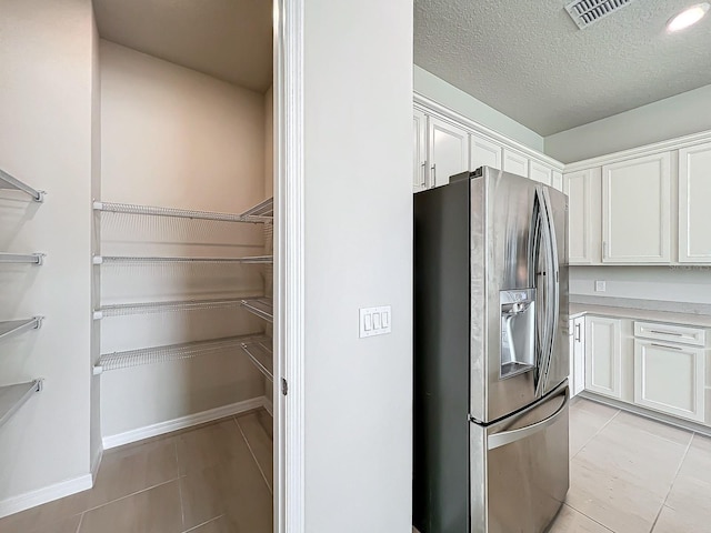 interior space with stainless steel fridge, white cabinets, and light tile patterned flooring