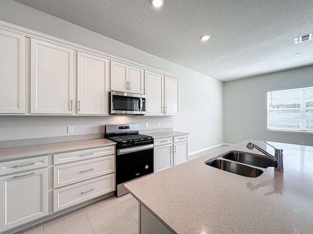 kitchen with light tile patterned floors, white cabinetry, a textured ceiling, sink, and stainless steel appliances