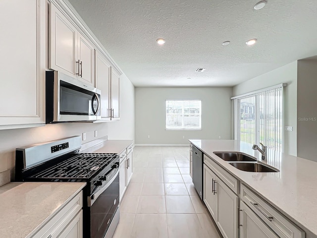 kitchen with stainless steel appliances, sink, light tile patterned floors, white cabinets, and a textured ceiling