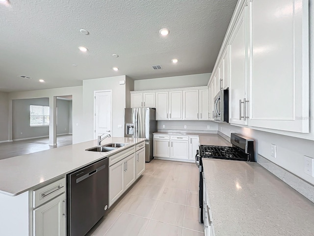 kitchen featuring stainless steel appliances, a center island with sink, sink, white cabinetry, and a textured ceiling