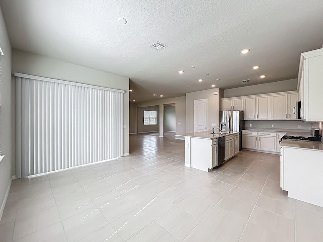 kitchen featuring a textured ceiling, stainless steel appliances, white cabinets, light tile patterned floors, and a kitchen island with sink